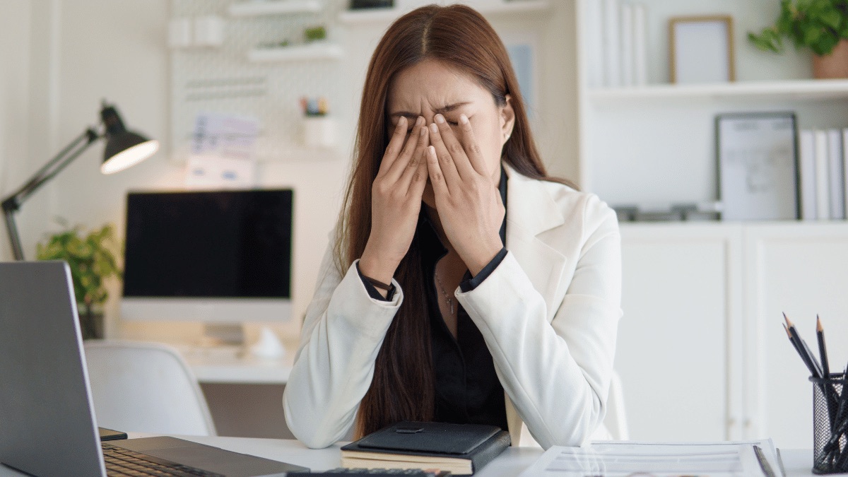 A professional overwhelmed at her desk with her hands over her face