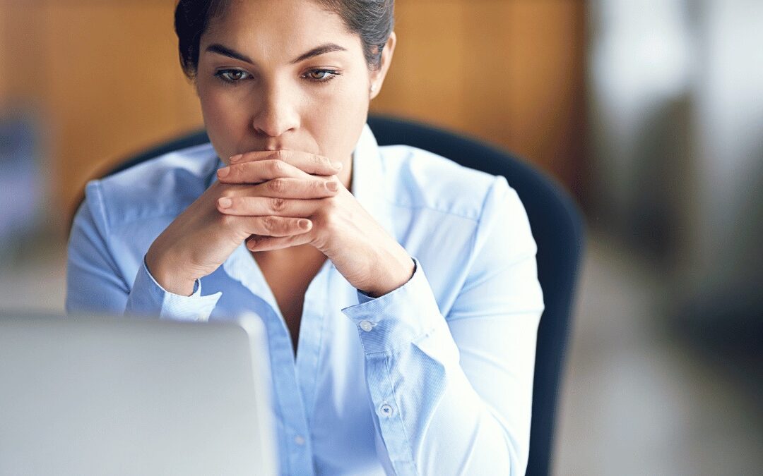 A professional sitting thoughtfully at her laptop under stress