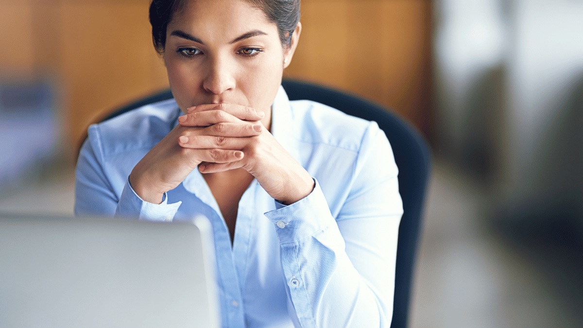 A professional sitting thoughtfully at her laptop under stress